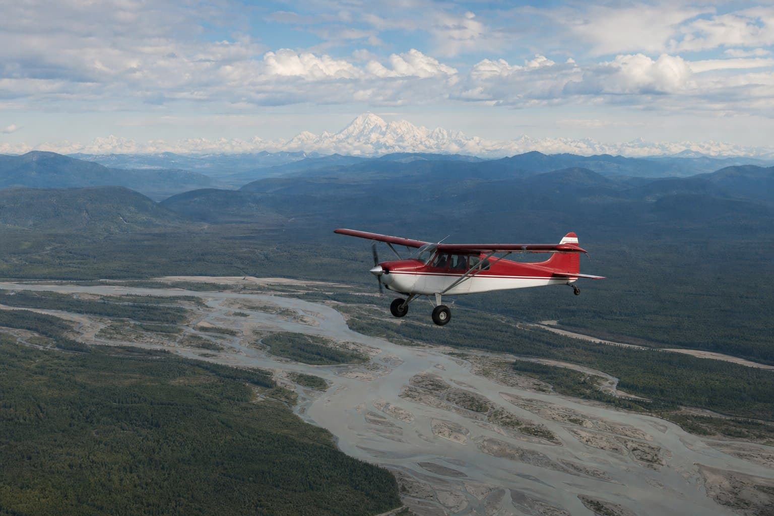 Small aircraft above braided Alaska river country and distant mountains