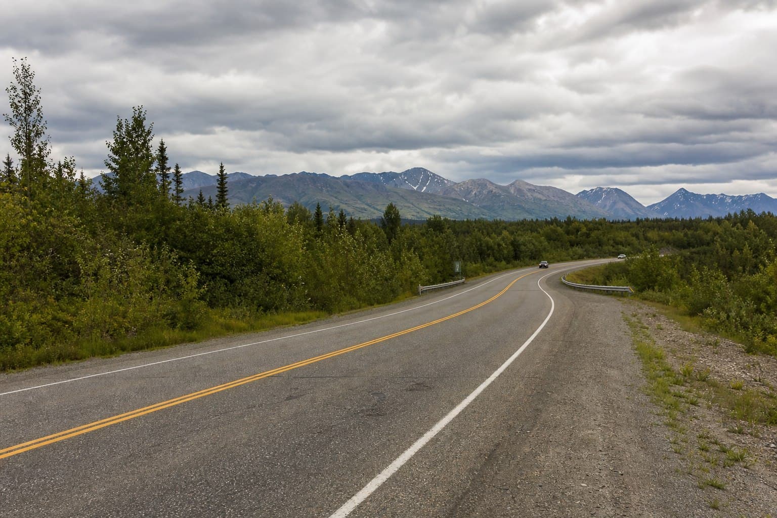 Two-lane Alaska highway through boreal foothills and distant mountains