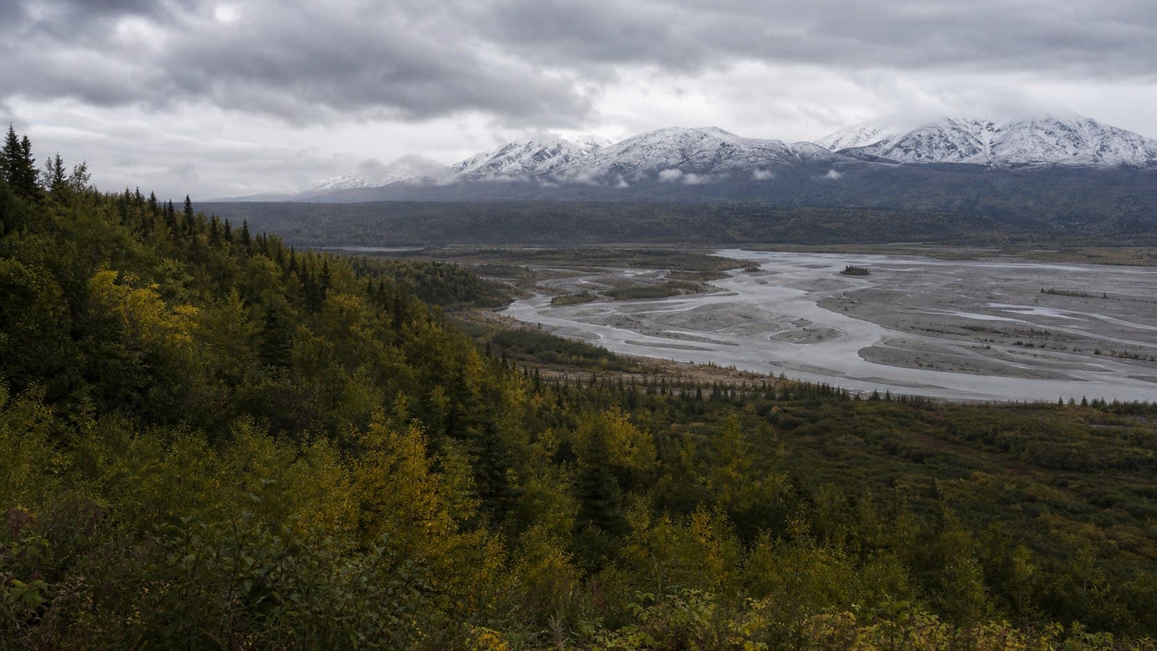 Braided river and snow-dusted mountains across an Alaska valley